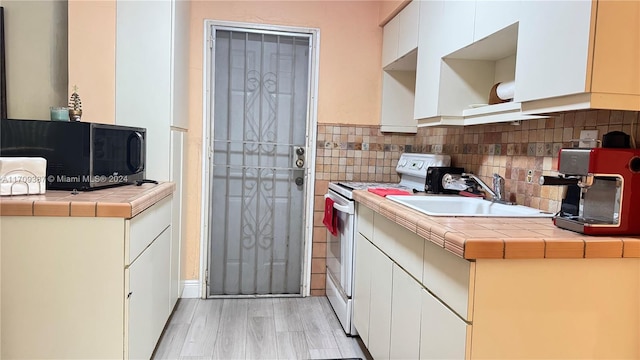 kitchen featuring light wood-type flooring, sink, tile countertops, white electric stove, and white cabinetry