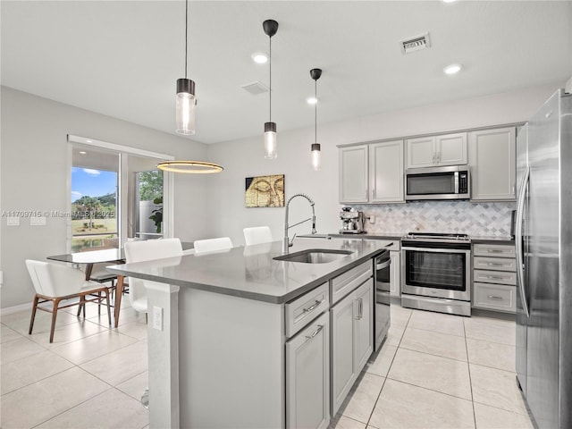 kitchen with hanging light fixtures, sink, stainless steel appliances, a center island with sink, and gray cabinets