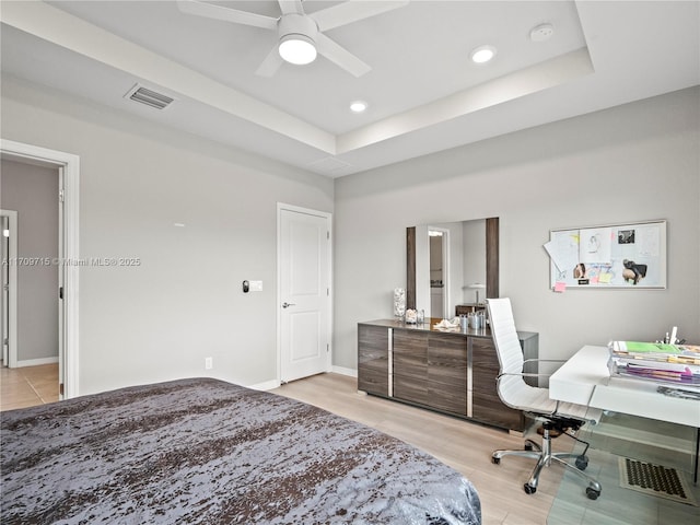 bedroom with ceiling fan, light hardwood / wood-style floors, and a tray ceiling