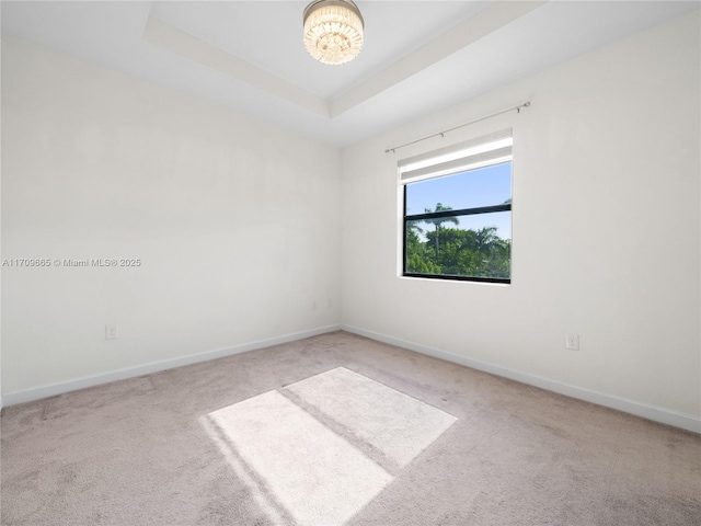 carpeted spare room featuring a raised ceiling and an inviting chandelier