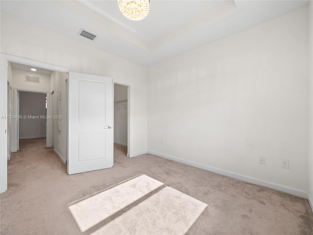 unfurnished bedroom with a tray ceiling, a spacious closet, a closet, and light colored carpet