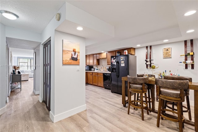 kitchen featuring a textured ceiling, sink, light hardwood / wood-style floors, and black appliances