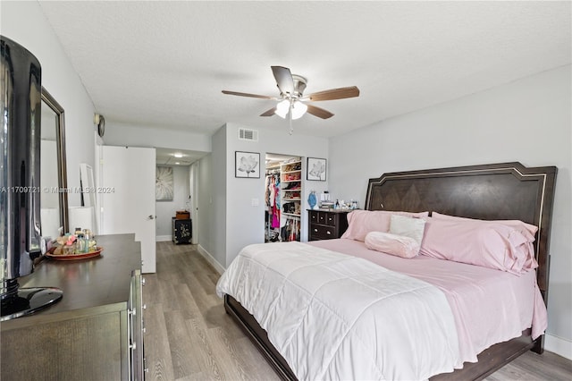 bedroom featuring a walk in closet, a textured ceiling, ceiling fan, light hardwood / wood-style floors, and a closet