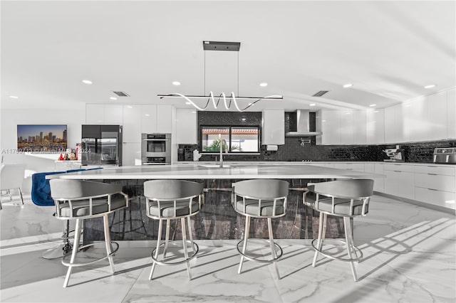 kitchen with black refrigerator, sink, wall chimney exhaust hood, decorative light fixtures, and white cabinetry