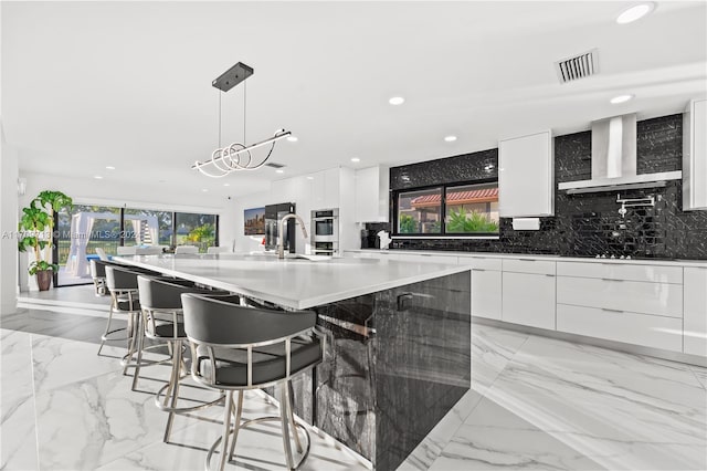 kitchen with white cabinetry, a spacious island, wall chimney range hood, and hanging light fixtures