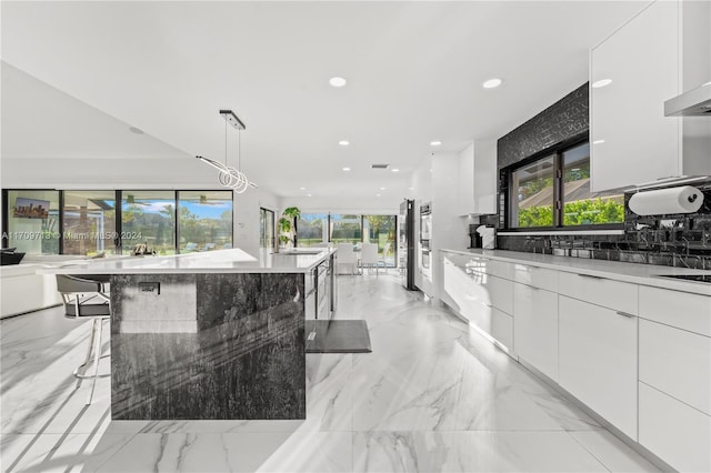 kitchen with decorative light fixtures, light stone countertops, a large island, white cabinetry, and a breakfast bar area