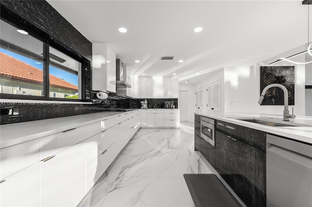 kitchen with wall chimney exhaust hood, stainless steel appliances, sink, decorative light fixtures, and white cabinets