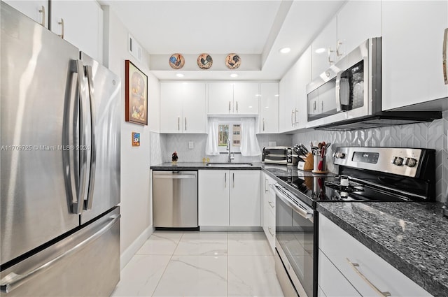 kitchen featuring dark stone counters, white cabinets, sink, decorative backsplash, and appliances with stainless steel finishes