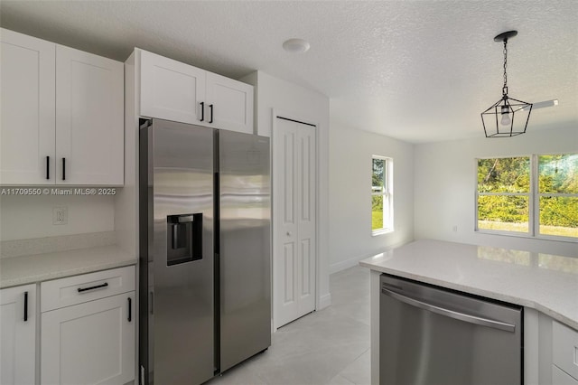 kitchen with light countertops, appliances with stainless steel finishes, hanging light fixtures, white cabinets, and a textured ceiling