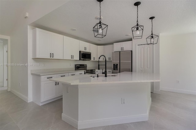 kitchen featuring a sink, appliances with stainless steel finishes, hanging light fixtures, white cabinetry, and a kitchen island with sink