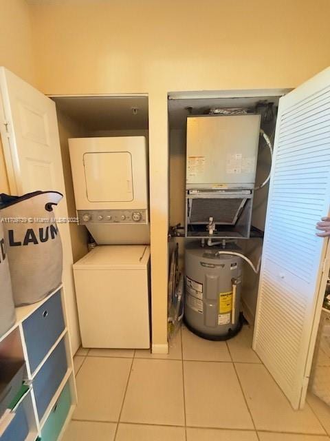 laundry area with electric water heater, light tile patterned floors, and stacked washer / drying machine