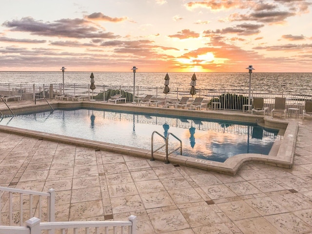 pool at dusk featuring a patio area and a water view