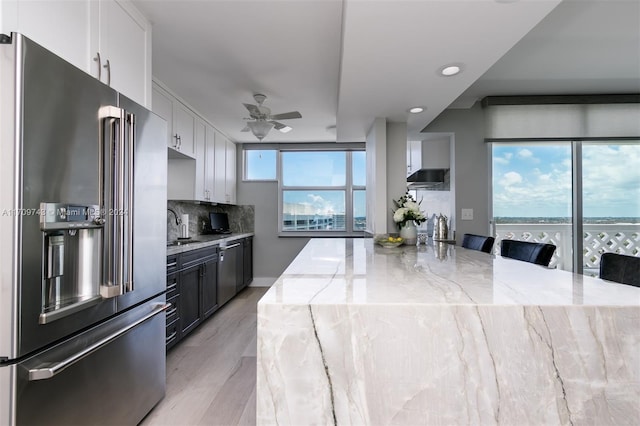 kitchen with backsplash, white cabinets, a kitchen breakfast bar, light wood-type flooring, and high end fridge