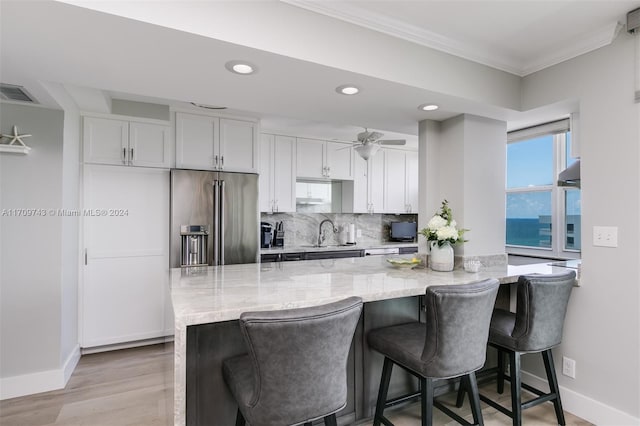 kitchen featuring a kitchen bar, high quality fridge, light stone countertops, and white cabinets