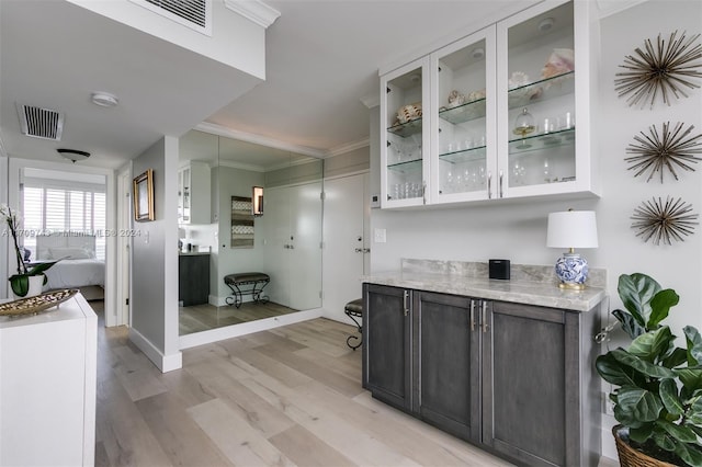 bar with white cabinets, light wood-type flooring, light stone countertops, and crown molding