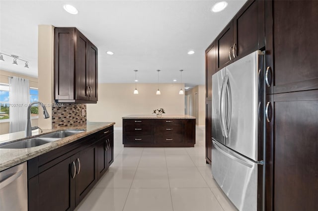 kitchen with sink, light stone counters, backsplash, decorative light fixtures, and appliances with stainless steel finishes