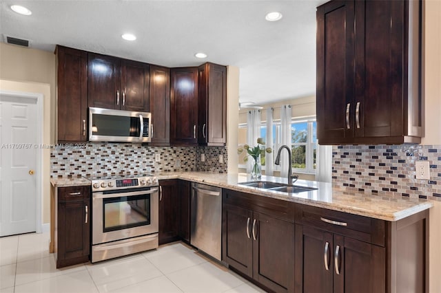 kitchen featuring sink, decorative backsplash, dark brown cabinets, light stone counters, and stainless steel appliances