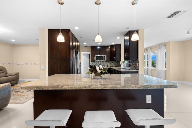 kitchen with light stone countertops, decorative backsplash, a breakfast bar, stainless steel appliances, and pendant lighting