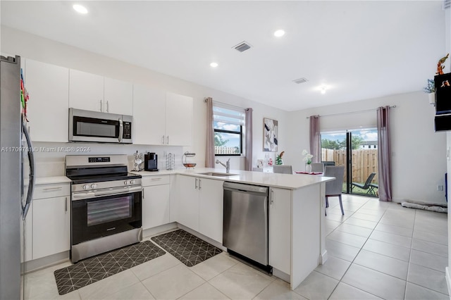 kitchen with white cabinets, sink, light tile patterned floors, appliances with stainless steel finishes, and kitchen peninsula