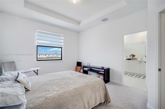 carpeted bedroom featuring ensuite bathroom and a raised ceiling