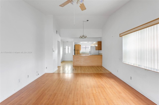 unfurnished living room with ceiling fan with notable chandelier, vaulted ceiling, and light wood-type flooring