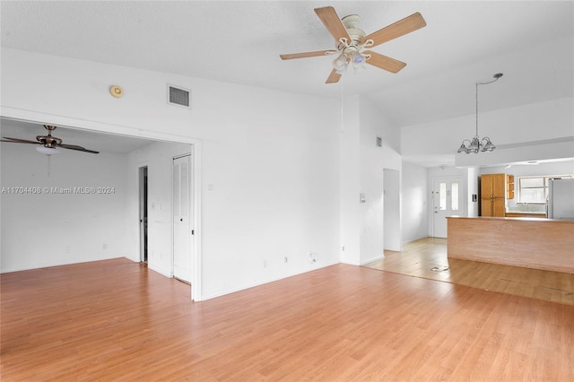 unfurnished living room with a textured ceiling, ceiling fan with notable chandelier, vaulted ceiling, and light wood-type flooring