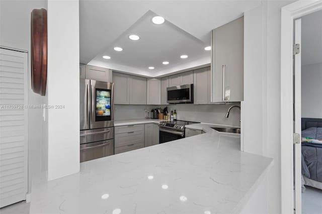 kitchen with kitchen peninsula, gray cabinetry, sink, and appliances with stainless steel finishes