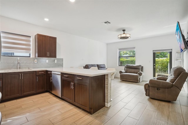 kitchen featuring sink, stainless steel dishwasher, decorative backsplash, light hardwood / wood-style floors, and kitchen peninsula