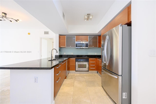 kitchen with backsplash, sink, dark stone countertops, appliances with stainless steel finishes, and kitchen peninsula