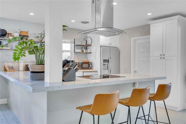 kitchen featuring white cabinetry, light stone countertops, island exhaust hood, stainless steel fridge, and kitchen peninsula