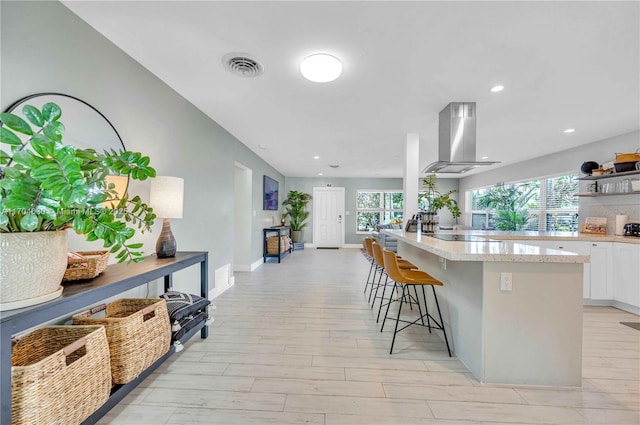 kitchen with island range hood, light wood-type flooring, white cabinetry, and a breakfast bar area