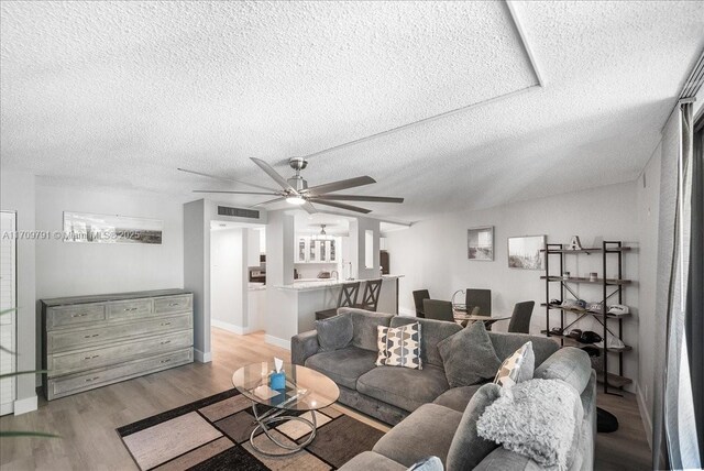 living room featuring ceiling fan, a textured ceiling, and light wood-type flooring