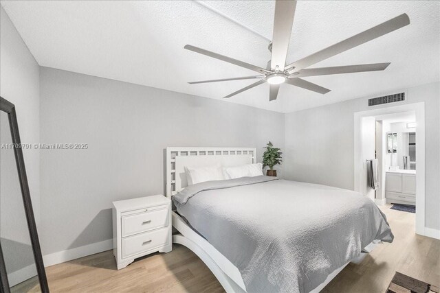 bedroom featuring ceiling fan, light hardwood / wood-style floors, a textured ceiling, and ensuite bath