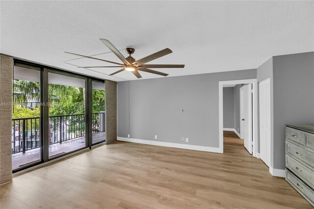 unfurnished room featuring ceiling fan, a wall of windows, a textured ceiling, and light hardwood / wood-style flooring