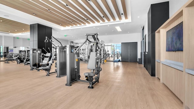 gym with a raised ceiling and light wood-type flooring