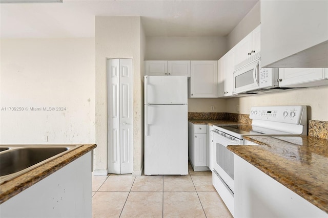 kitchen with white cabinetry, light tile patterned floors, dark stone counters, and white appliances