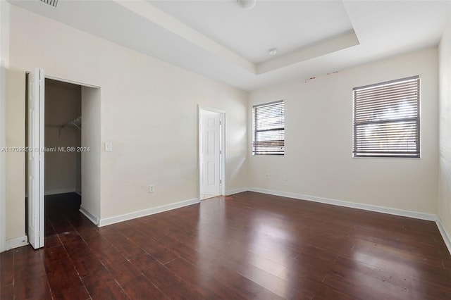 unfurnished bedroom with a walk in closet, dark hardwood / wood-style flooring, a raised ceiling, and a closet