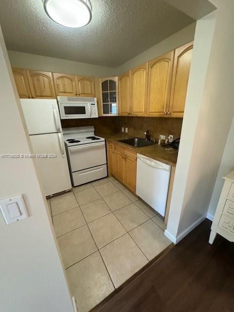 kitchen featuring white appliances, light tile patterned floors, light brown cabinets, a textured ceiling, and sink