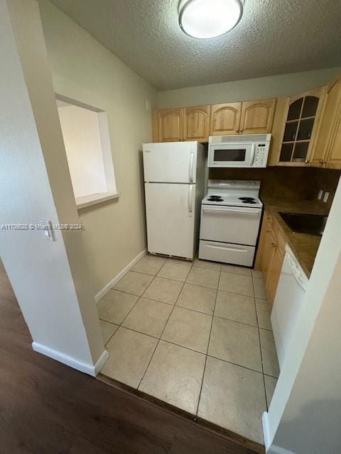 kitchen with white appliances, a textured ceiling, light tile patterned floors, and light brown cabinets