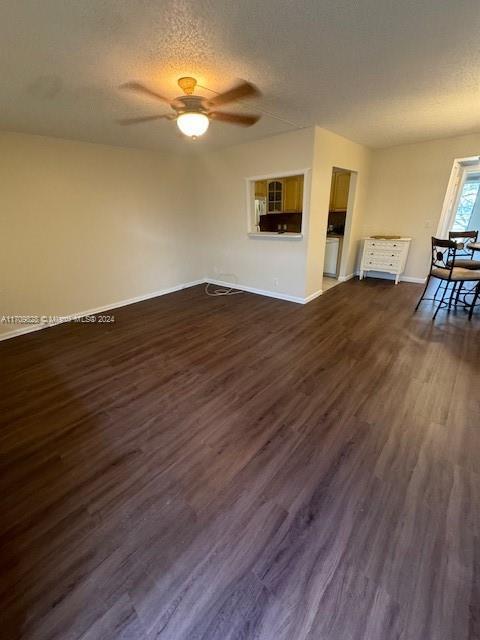 unfurnished living room featuring a textured ceiling, ceiling fan, and dark wood-type flooring