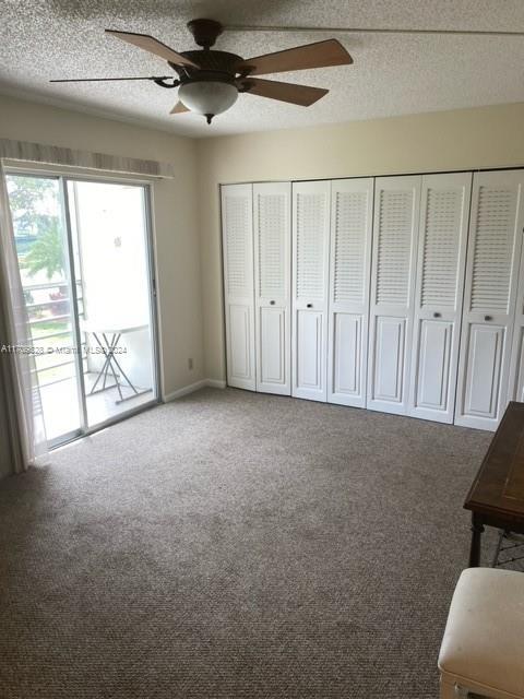 unfurnished bedroom with carpet flooring, access to exterior, ceiling fan, and a textured ceiling