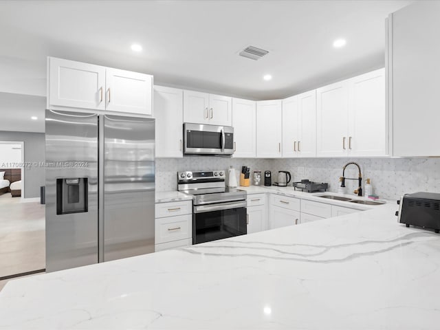 kitchen with white cabinets, appliances with stainless steel finishes, light stone counters, and sink