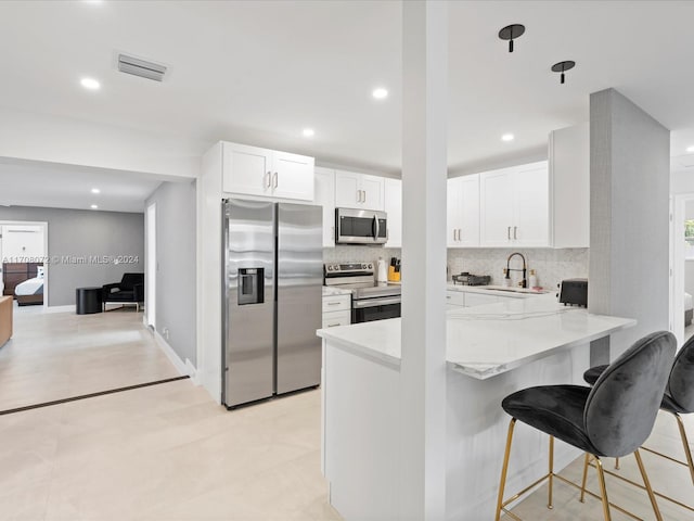 kitchen with backsplash, kitchen peninsula, a breakfast bar area, white cabinets, and appliances with stainless steel finishes