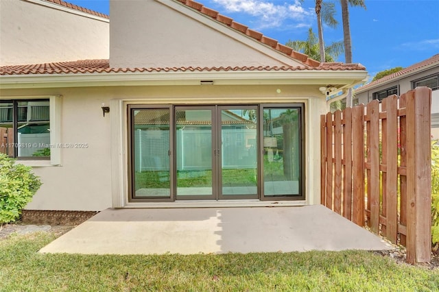 view of exterior entry with stucco siding, a tile roof, and fence