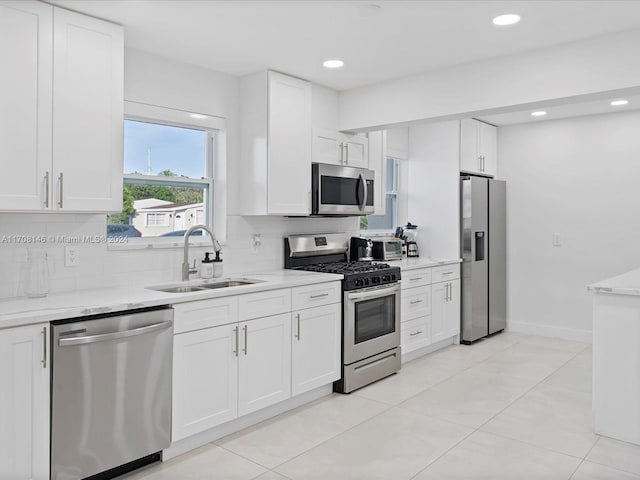 kitchen featuring light stone countertops, backsplash, stainless steel appliances, sink, and white cabinets