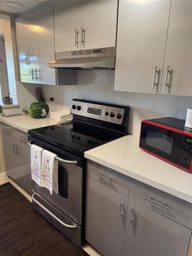 kitchen with gray cabinetry, backsplash, stainless steel range with electric cooktop, light hardwood / wood-style flooring, and light stone counters