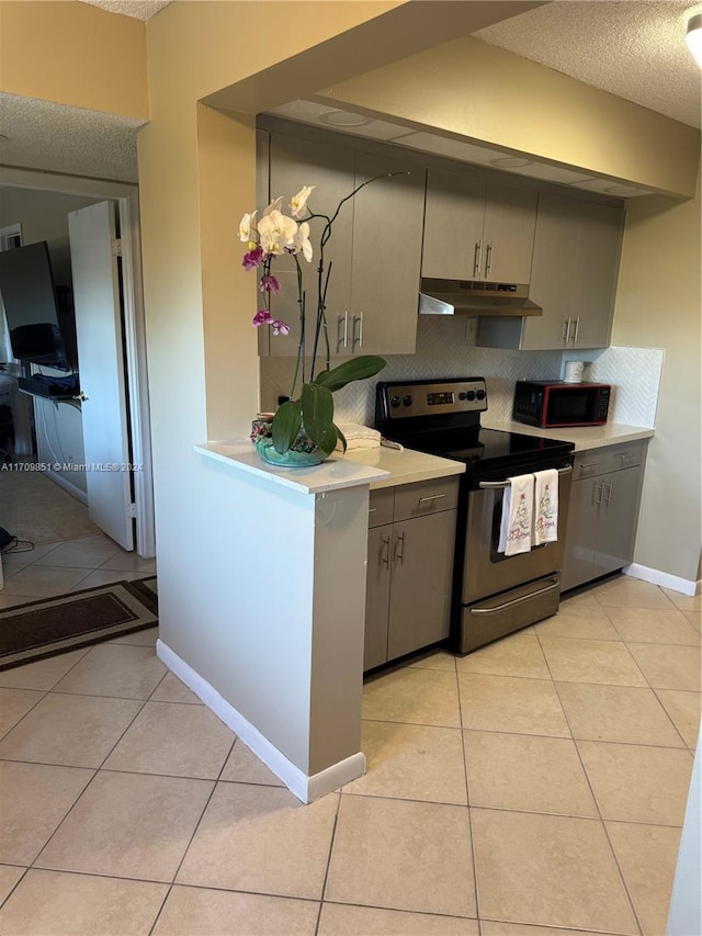 kitchen with stainless steel electric range, backsplash, gray cabinets, light tile patterned floors, and a textured ceiling