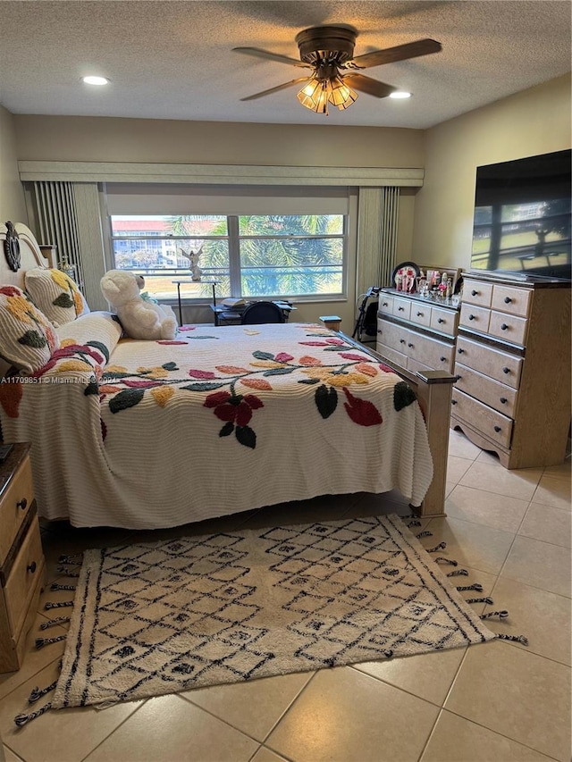 bedroom featuring ceiling fan, light tile patterned floors, and a textured ceiling