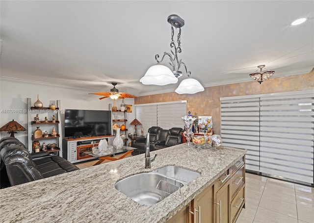 kitchen with decorative light fixtures, ornamental molding, open floor plan, a sink, and light stone countertops