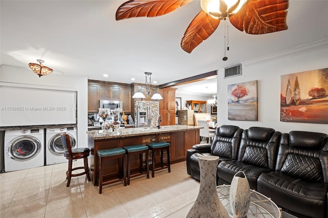 living area featuring crown molding, a notable chandelier, light tile patterned floors, visible vents, and independent washer and dryer